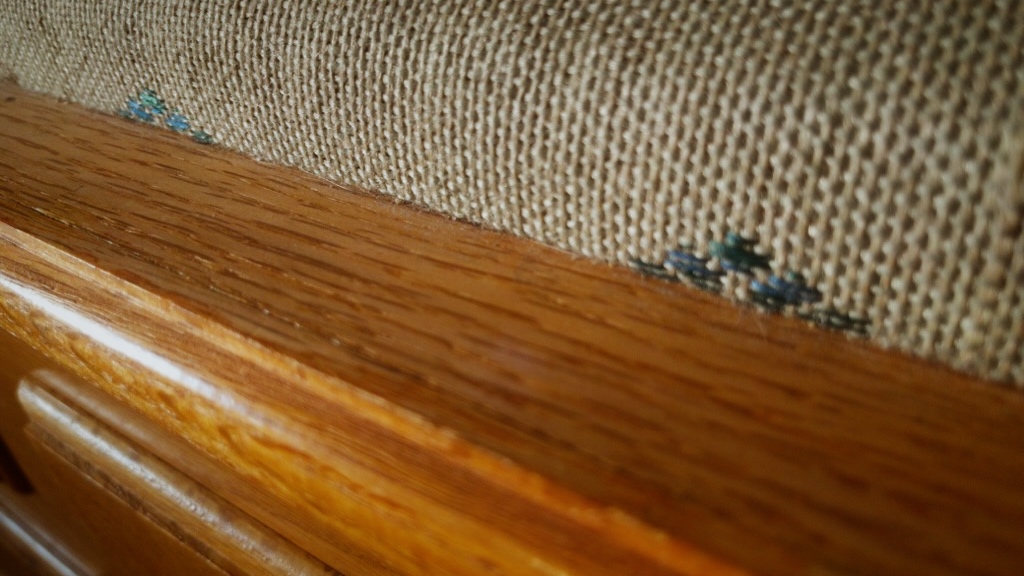 Close-up photo of worn woven upholstery meeting a polished wooden furniture frame.